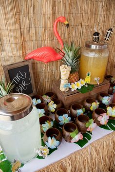 a table topped with pineapples and cups filled with liquid next to a flamingo