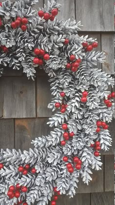 a christmas wreath with red berries and pine cones on a wooden fence next to a brick wall