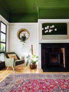 a living room with green walls and a rug on the floor in front of a fireplace