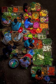 an overhead view of several people sitting at tables with baskets of vegetables and fruit on the ground