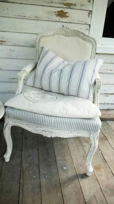 an old white chair with blue and white striped pillows on it's back end