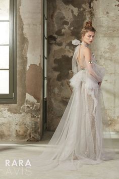 a woman in a white wedding dress standing next to an old brick wall and window