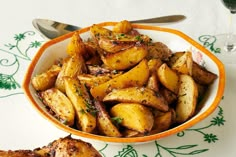 a bowl filled with cooked potatoes on top of a table next to a glass of wine