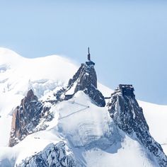 a mountain covered in snow with a building on it's top and some mountains behind it