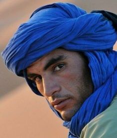 a man wearing a blue turban looks off to the side with his eyes wide open