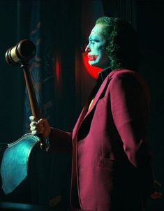 a woman dressed as the joker holding a hammer in a dark room with red lights