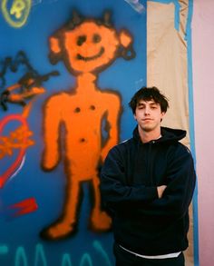 a man standing in front of a graffiti wall with his arms crossed and looking at the camera