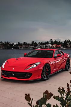 a red sports car parked next to a body of water with palm trees in the background