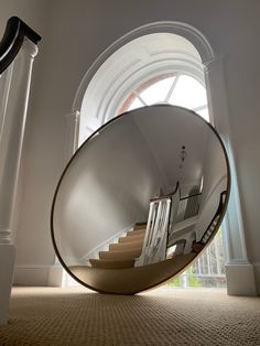 a circular mirror sitting in the middle of a hallway next to a stair case and window