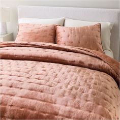 a bed with pink comforter and pillows on top of the headboard in a bedroom