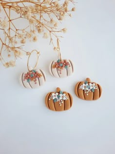 three decorated pumpkin shaped cookies sitting on top of a white table next to dried flowers