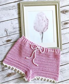 a pink crocheted shorts with white trim is next to a framed photograph on a wooden surface