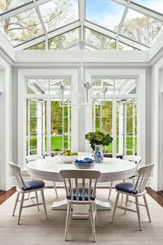 a white dining room table surrounded by glass doors and windows that look out onto the garden