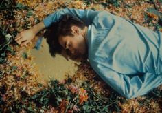 a man laying on the ground surrounded by leaves and flowers with his eyes closed, looking down