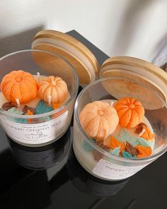 two glass bowls filled with small pumpkins on top of a black table next to a white wall