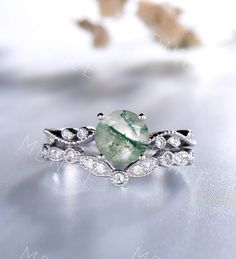 a ring with a large green stone surrounded by white diamonds on a silver surface next to flowers