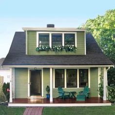 a green house with white trim and two chairs on the front porch, next to a wooden walkway