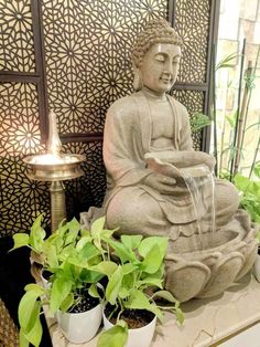 a buddha statue sitting on top of a table next to potted plants and a lamp