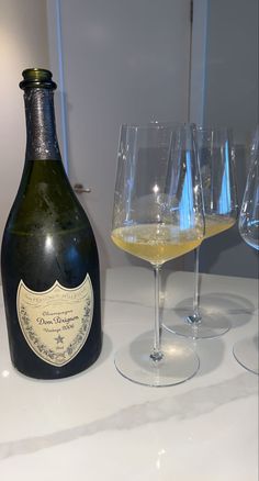 a bottle of wine next to three glasses on a counter with white walls in the background