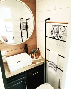 a white toilet sitting next to a bathroom sink under a round mirror in a bathroom