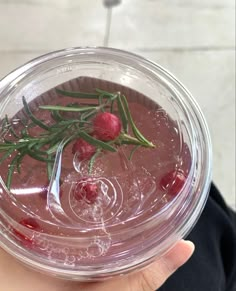 a person holding up a glass bowl filled with liquid and cranberry garnish