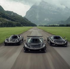 three supercars driving down a road in the middle of mountains and grass on either side