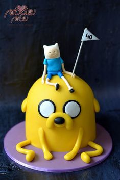 a yellow cake with a cartoon character on top and a flag sticking out of it