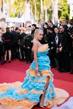 a woman in a blue and yellow dress standing on a red carpet with cameras surrounding her