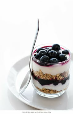 a dessert with blueberries and granola in a glass bowl on a white plate