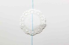 a white doily hanging from a blue string on a wall next to a piece of paper