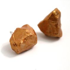 two gold nuggets sitting next to each other on top of a white surface