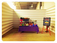 a woman standing behind a purple table with food on it