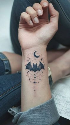 a woman's arm with a bat and stars tattoo on the left side of her wrist