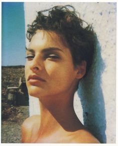 a young woman leaning against a wall with her eyes closed and hair blowing in the wind