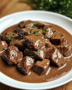 a white plate topped with meat and gravy on top of a wooden table