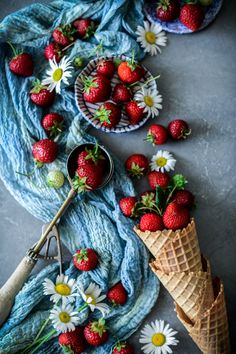 strawberries and daisies are arranged in cones on a table next to blue yarn