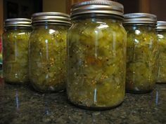 four jars filled with pickles sitting on top of a counter