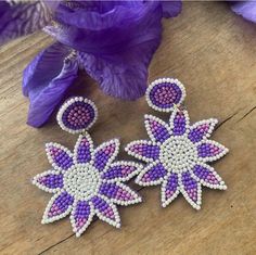 two purple and white beaded earrings on top of a wooden table next to flowers