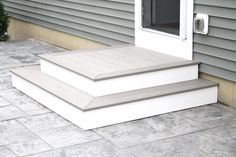 two steps leading up to a door on the side of a house with grey siding