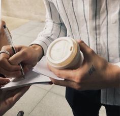 two people are holding coffee cups and writing on paper