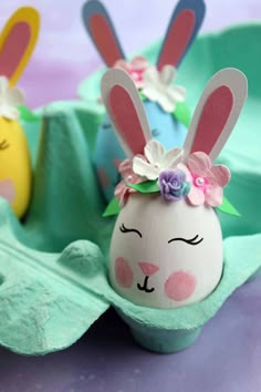 two decorated eggs in an egg carton with bunny ears and flowers on their heads