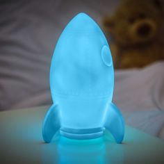 a blue light up rocket sitting on top of a table next to a teddy bear