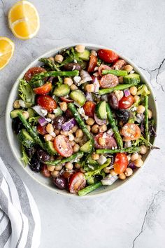 a white bowl filled with beans, asparagus and tomatoes on top of a marble table