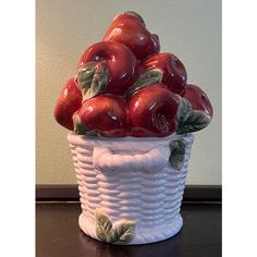 a white basket filled with red apples sitting on top of a wooden table next to a wall