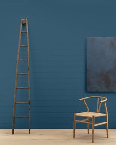 a ladder leaning against a blue wall next to a chair and painting on the wall