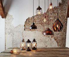 several lights hanging from the ceiling over a wooden table in front of a brick wall