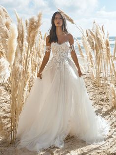 a woman in a white wedding dress standing on the beach with pamodia grass