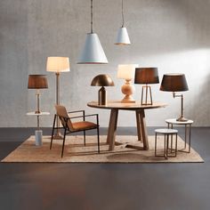 a table with lamps and chairs around it on a rug in front of a wall