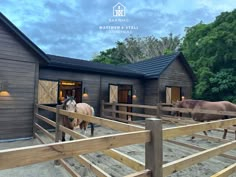 two horses are standing in front of a barn with wooden doors and windows on the side