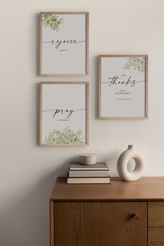 three framed art prints on the wall above a dresser with books and vase in front